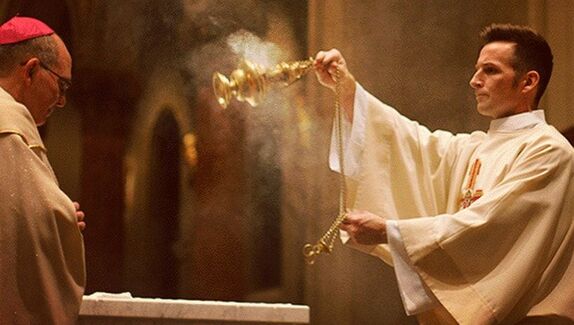 A picture of a priest facing left swinging a gold thurible with incense plumes coming out and an archbishop on the right.