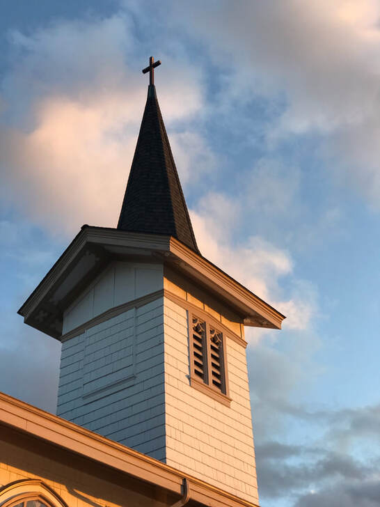 A picture of the steeple of Sacred Heart Catholic Church in Bellingham, Washington. The sky is partly cloudy behind it.
